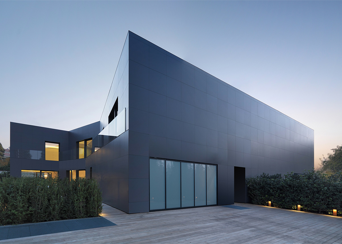 Casa moderna e minimalista con pannelli scuri eleganti, ampie finestre e illuminazione soffusa, circondata dal verde