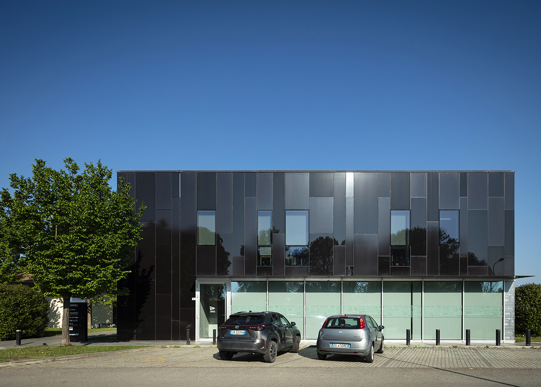 Edificio moderno nero con pannelli riflettenti e finestre verticali, sotto un cielo azzurro e limpido.