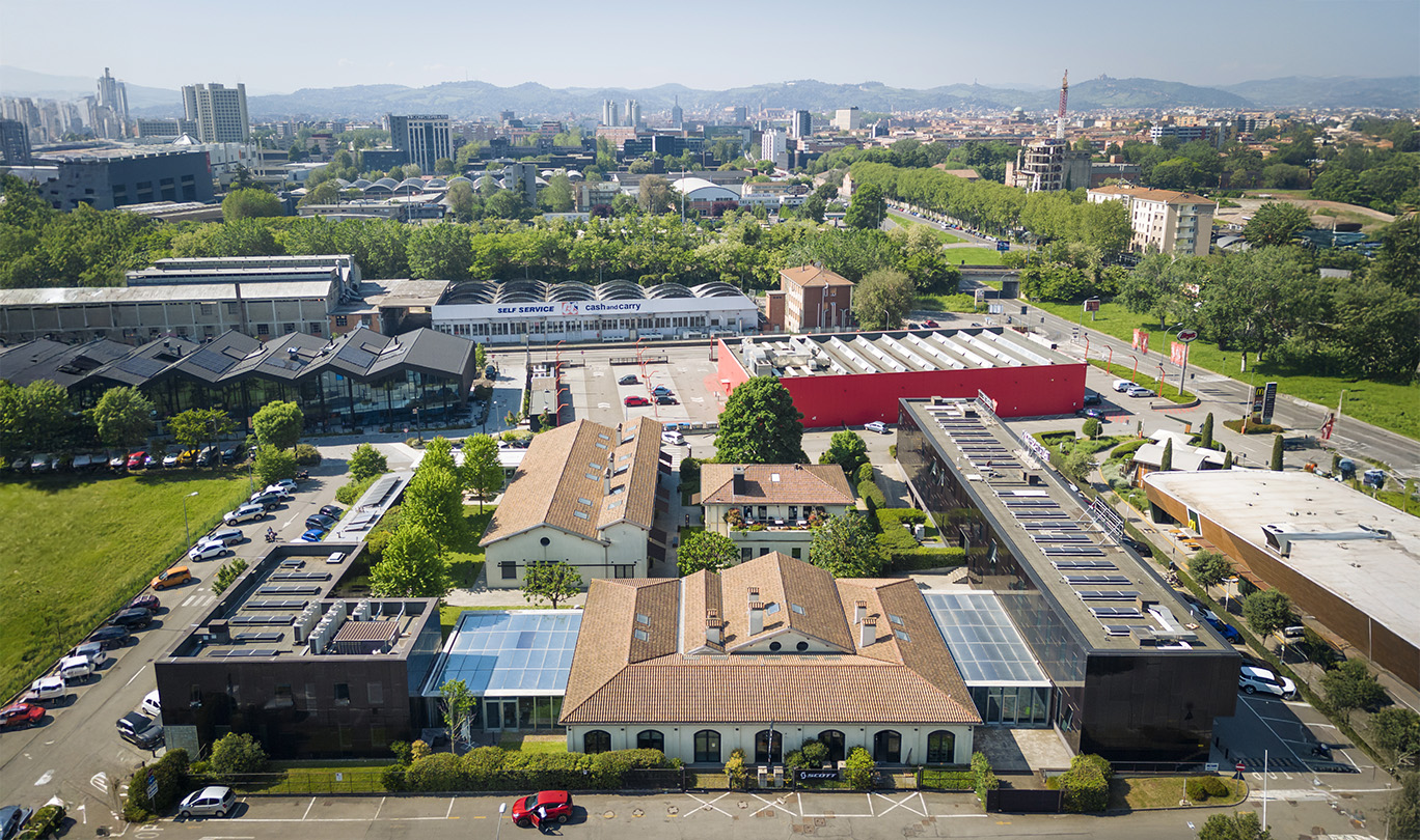 Veduta aerea di un ampio complesso commerciale, circondato dal verde e da parcheggi. Sullo sfondo il paesaggio urbano.