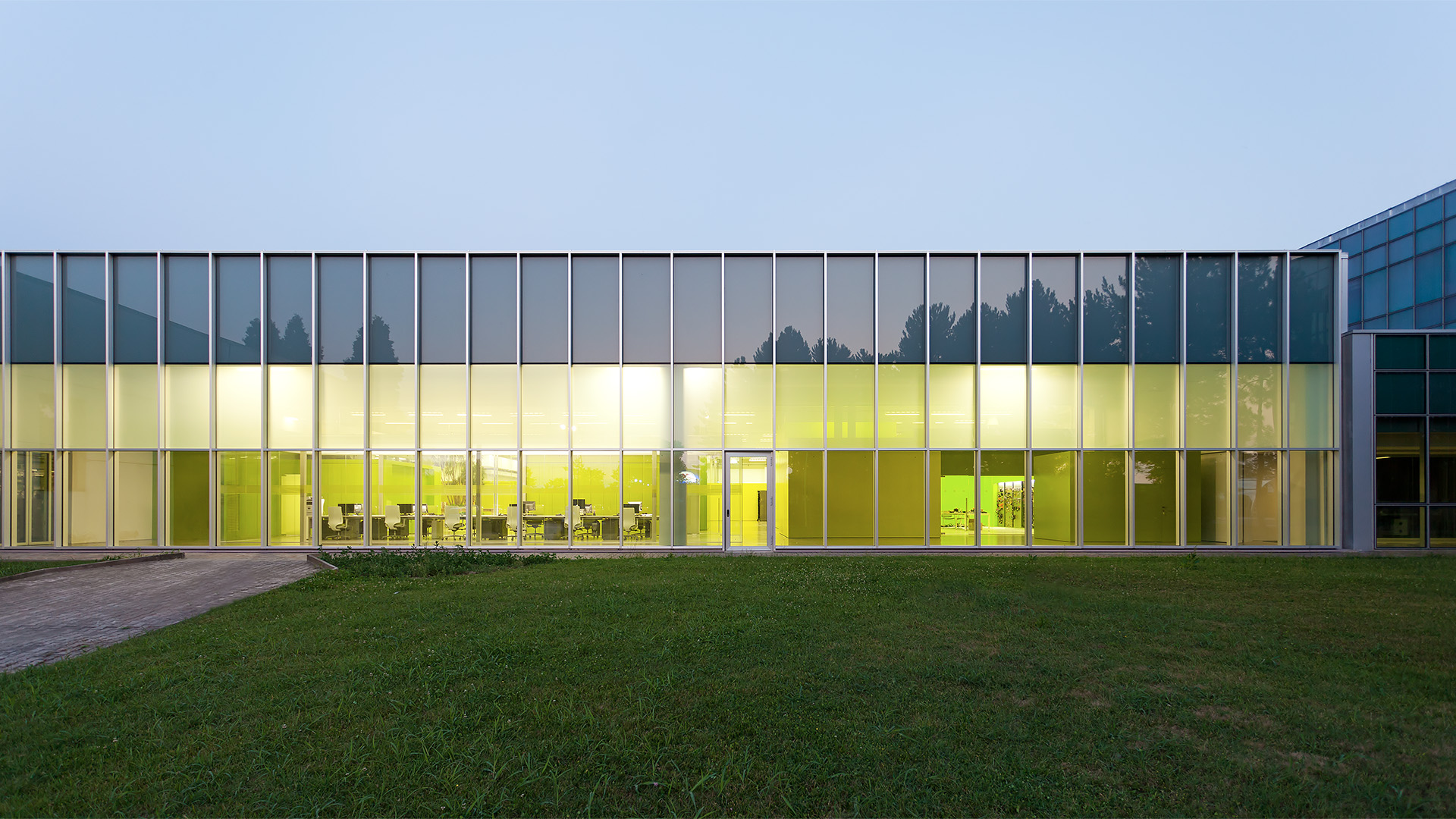 Edificio moderno con pareti di vetro verde e un ampio prato verde
