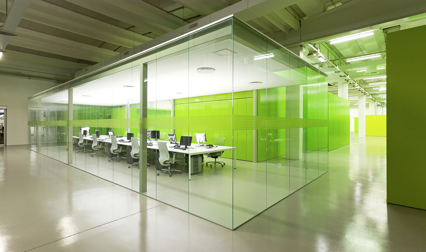 Sala riunioni con parete di vetro e scrivanie in un ambiente verde, ideale per stimolare la creatività e la produttività